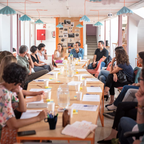 Vista frontal de 16 personas alrededor de una mesa en un taller sobre maternidad y DCA.